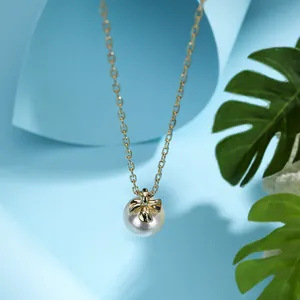 Gold chain necklace with a pearl pendant and bow detail on a tropical leaf background
