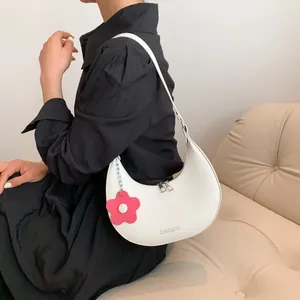 White crescent moon shoulder bag with silver zippers and a red floral charm accessory