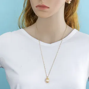 Detail view of a long gold necklace with large pearl pendant and matching stud earrings