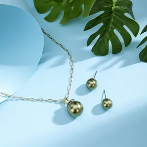 Detail of gold necklace and olive green pearl earrings on a light blue background