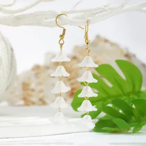 Detail of hanging lily of the valley earrings with white resin flowers and gold hooks
