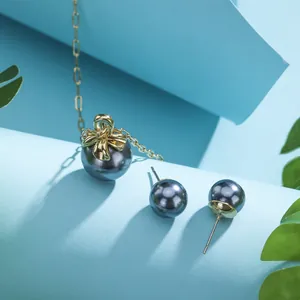 Detail of gold necklace and pearl earrings set with bow accents on blue background