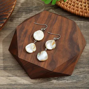 Detail view of handmade shell earrings with iridescent luster on wooden display stand