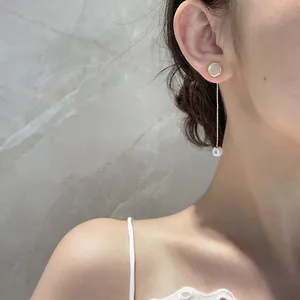 Detail of long gold tassel earring with white pearl and opal stone on a model