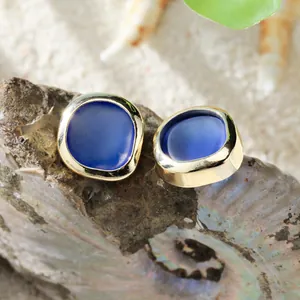 Bohemian gold plated sea glass stud earrings with dark blue stone on sandy beach background