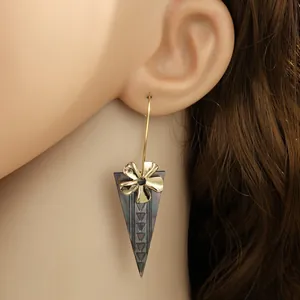 Detail eines goldenen Blumenohrrings mit schwarzem Muschel-Dreiecksanhänger am Model