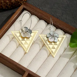 Nahaufnahme goldener Edelstahlohrringe mit geometrischem Dreieck und Muschelblume