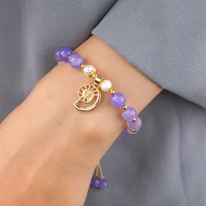 Bracelet élégant en améthyste et perles avec breloque coquillage doré au poignet féminin