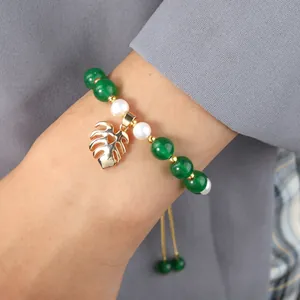 Close-up of pearl bracelet with green beads and gold monstera leaf charm detail
