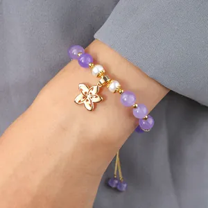 Détail du bracelet en améthyste et perles avec pendentif fleur dorée sur le poignet