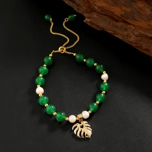 Detailed shot of green jade beads and pearl bracelet with a golden monstera leaf charm