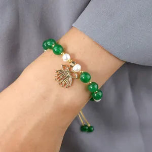 Detail of adjustable pearl and green jade bracelet with textured golden leaf pendant