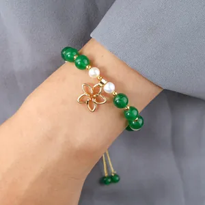 Detail of green jade and pearl bracelet with golden flower charm on a wrist