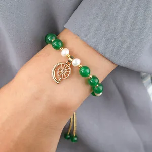 Elegant green jade and pearl bracelet with golden spiral pendant on grey background