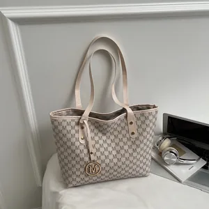 Chic M-patterned tote bag with gold metal charm on a desk with headphones