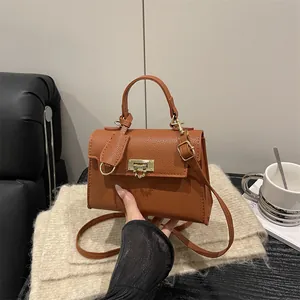 Braune Handtasche aus Leder mit goldener Schließe und verstellbarem Riemen in warmer Szene