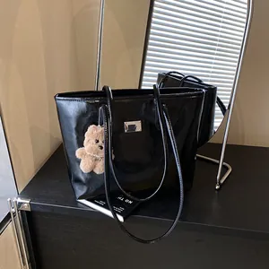 Glossy black leather tote bag with a small plush bear charm in a chic indoor setting