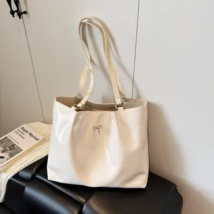 Chic beige patent leather tote bag with silver bow accent and elegant pleated design