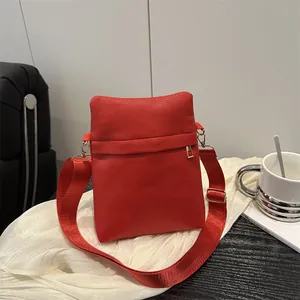 Elegant red pebbled leather shoulder bag with gold hardware and nylon strap on a white cloth