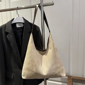 Minimalist beige suede tote bag with brown leather straps shown on a metal stand