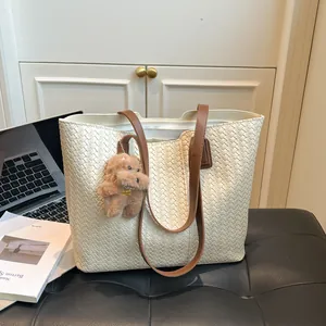 Minimalist woven tote bag with brown leather straps and a plush dog pendant charm