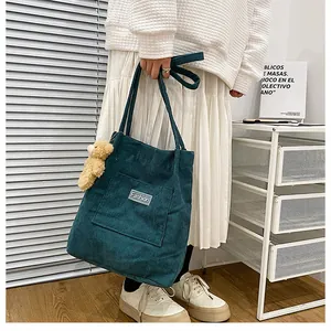 Detail of dark green corduroy tote bag with plush bear charm and Fashion label