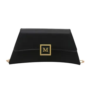 Minimalist black trapezoid pillow bag with golden M-logo and chain strap for women