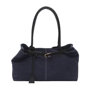Borsa tote in denim blu con manici neri e fibbia in metallo su sfondo bianco