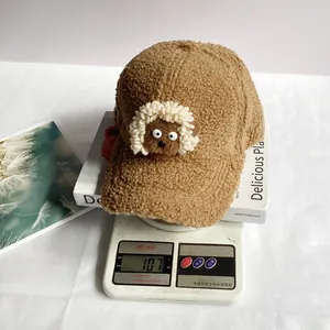 Détail d'une casquette en peluche marron avec agneau 3D posée sur une balance