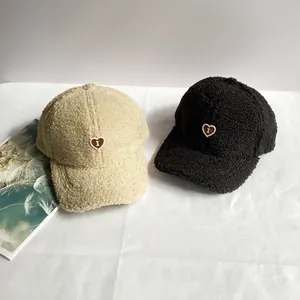Dettaglio del ricamo a cuore sui berretti da baseball in lana di agnello beige e nero