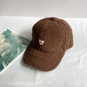 Nahaufnahme der braunen Teddy-Fleece-Kappe mit weißem Bären-Stick und M-Logo-Detail