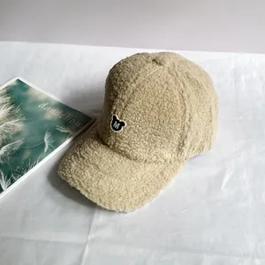 Nahaufnahme der flauschigen Lammwoll-Struktur und M-Buchstaben Stickerei auf der beigen Kappe