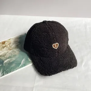 Dettaglio del cappello da baseball in pile nero con trama morbida e toppa a cuore