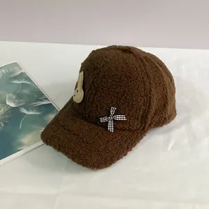 Détail d'une casquette en peluche marron avec écusson lapin et petit nœud à carreaux