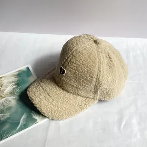 Dettaglio ravvicinato del cappellino beige in pile con toppa a cuore e bordo di perle