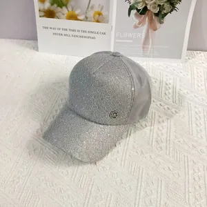 Close-up of gray baseball cap featuring floral lace overlay with shimmering sequins and MC logo
