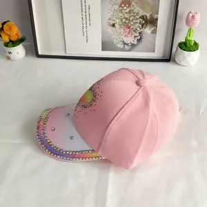Close-up of pink baseball cap featuring rainbow sequin heart and colorful rhinestones on brim