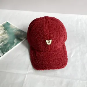 Detail der roten Fleece-Baseballkappe mit M-Buchstaben-Bärenstickerei und weicher Textur