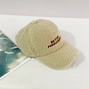 Detailed view of beige faux shearling baseball cap with dark brown letter embroidery