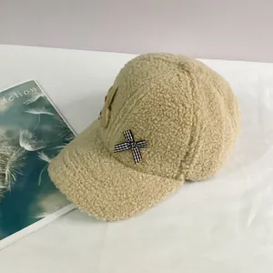 Détail de la casquette beige en polaire avec nœud à carreaux et écusson lapin mignon