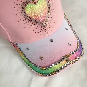 Close-up of pink baseball cap featuring a glitter heart and rhinestone-studded rainbow brim