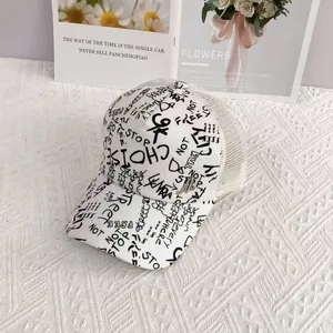 Close-up of white mesh trucker hat featuring black graffiti prints and metal M logo