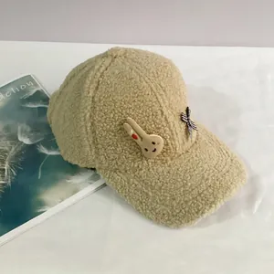 Détail de la casquette beige en polaire sherpa avec broche lapin et nœud à carreaux