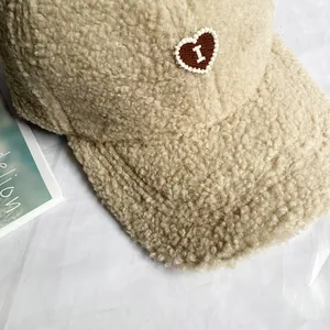 Dettaglio del cappello beige in pile con toppa a cuore marrone e ricamo riccio