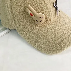 Détail d'une casquette beige en sherpa avec écusson lapin et nœud à carreaux élégant