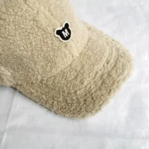 Detailaufnahme der beigen Fleece-Baseballkappe mit M-Logo-Stickerei und Bären-Aufnäher