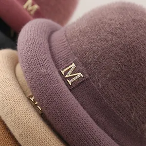 Detail of soft knit bucket hat with curly brim and sparkling rhinestone M metal emblem