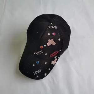 Close-up of sparkling rhinestone LOVE letters and red sequin lip on a black baseball cap