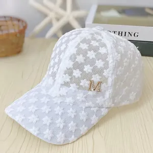 Close-up of white floral lace embroidery and gold metal M logo on breathable mesh cap