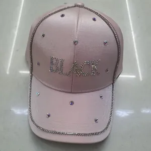 Dettaglio del cappello da baseball in raso rosa chiaro con scritta BLACK in strass